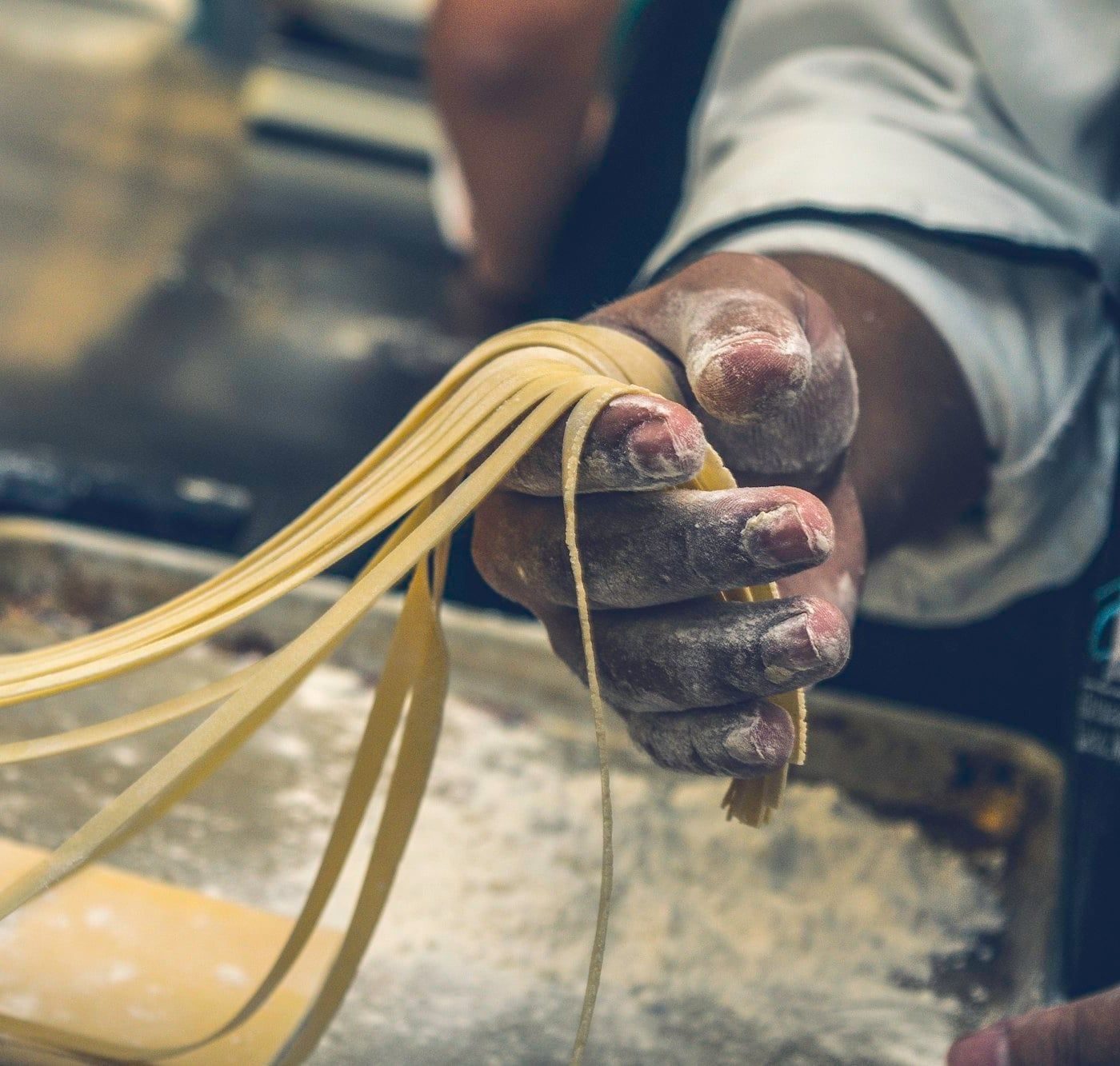 Manos levantando tagliatelle recién cortadas sobre una superficie enharinada